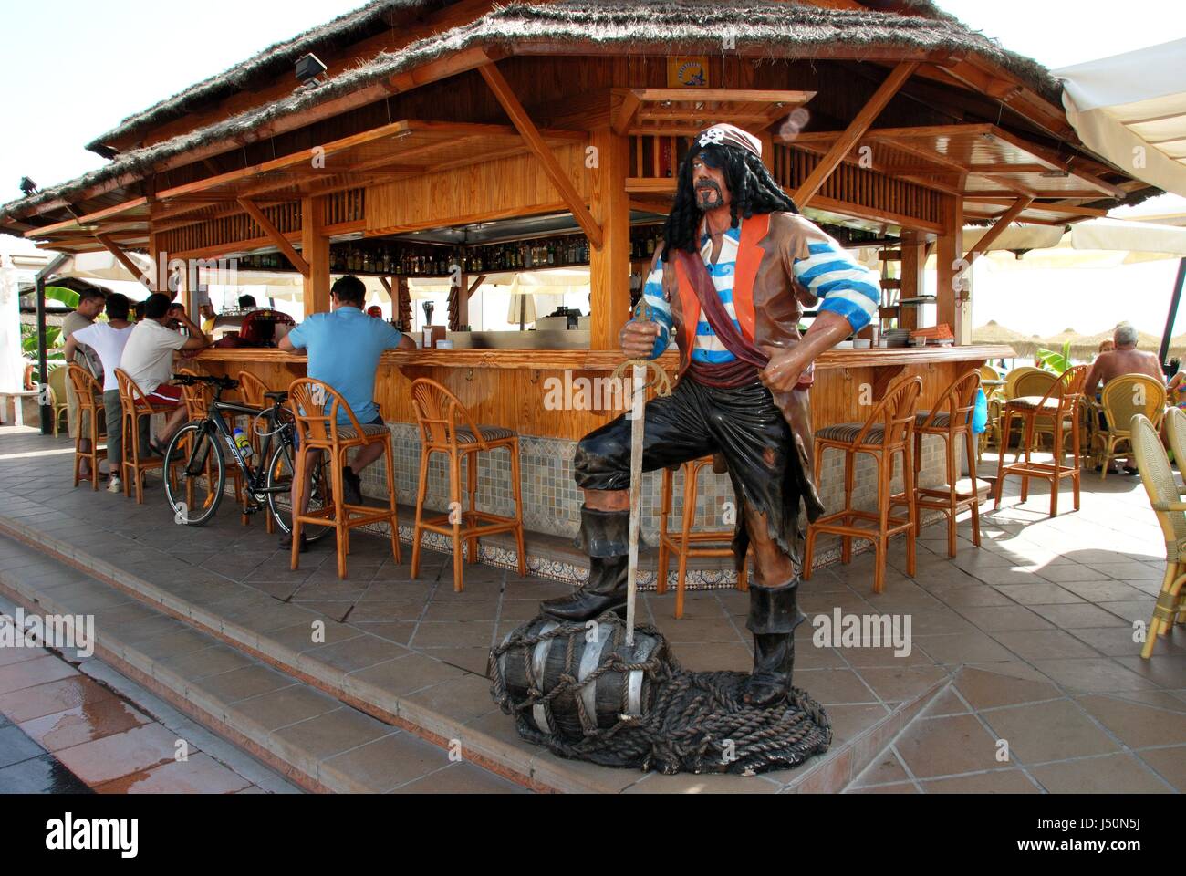Tourists relaxing at a beach bar along the promenade with a pirate statue in the foreground, Torremolinos, Malaga Province, Andalusia, Spain, Western  Stock Photo