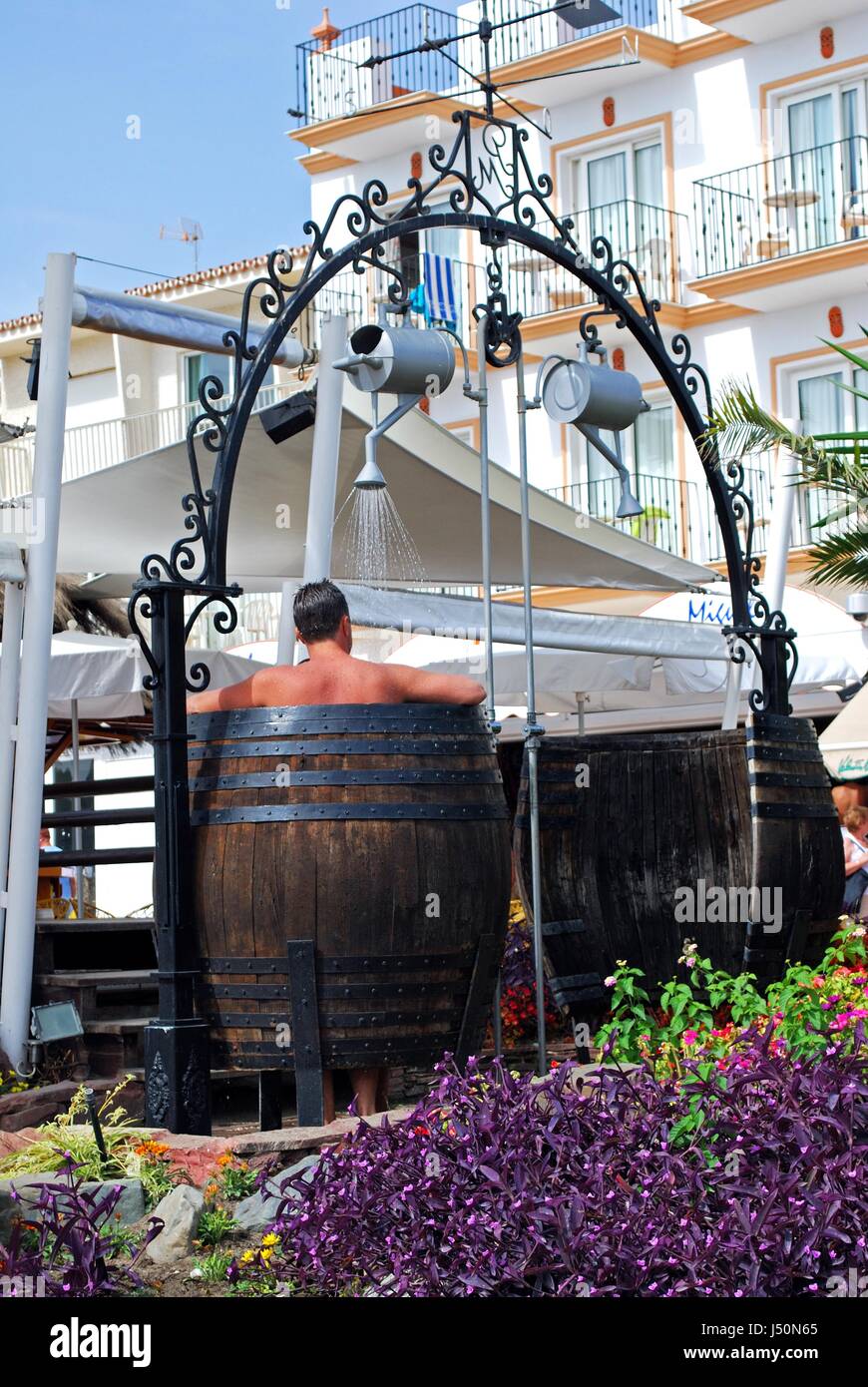 Man taking a shower in a barrel beach shower outside beach bar