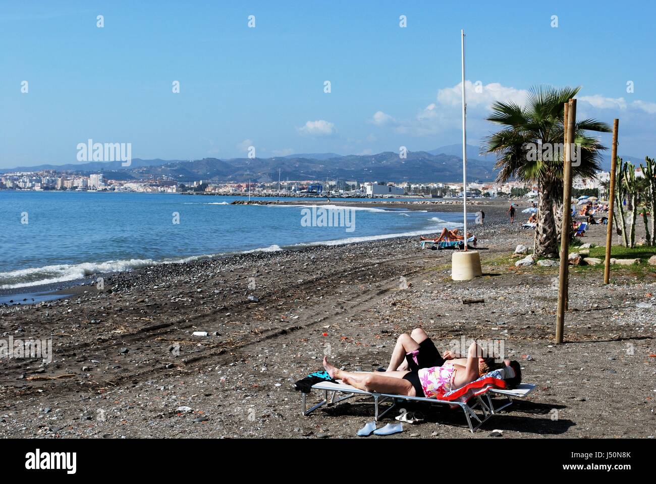 Tourists relaxing on the pebble beach with views along the coastline, Lagos, Malaga Province, Andalusia, Spain, Western Europe. Stock Photo
