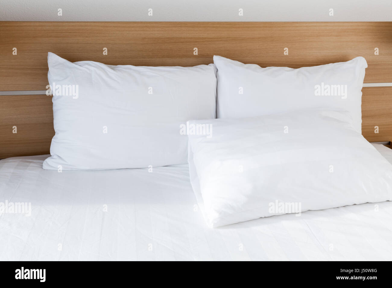 White pillows lay on wide empty bed with wooden headboard, bedroom interior fragment Stock Photo