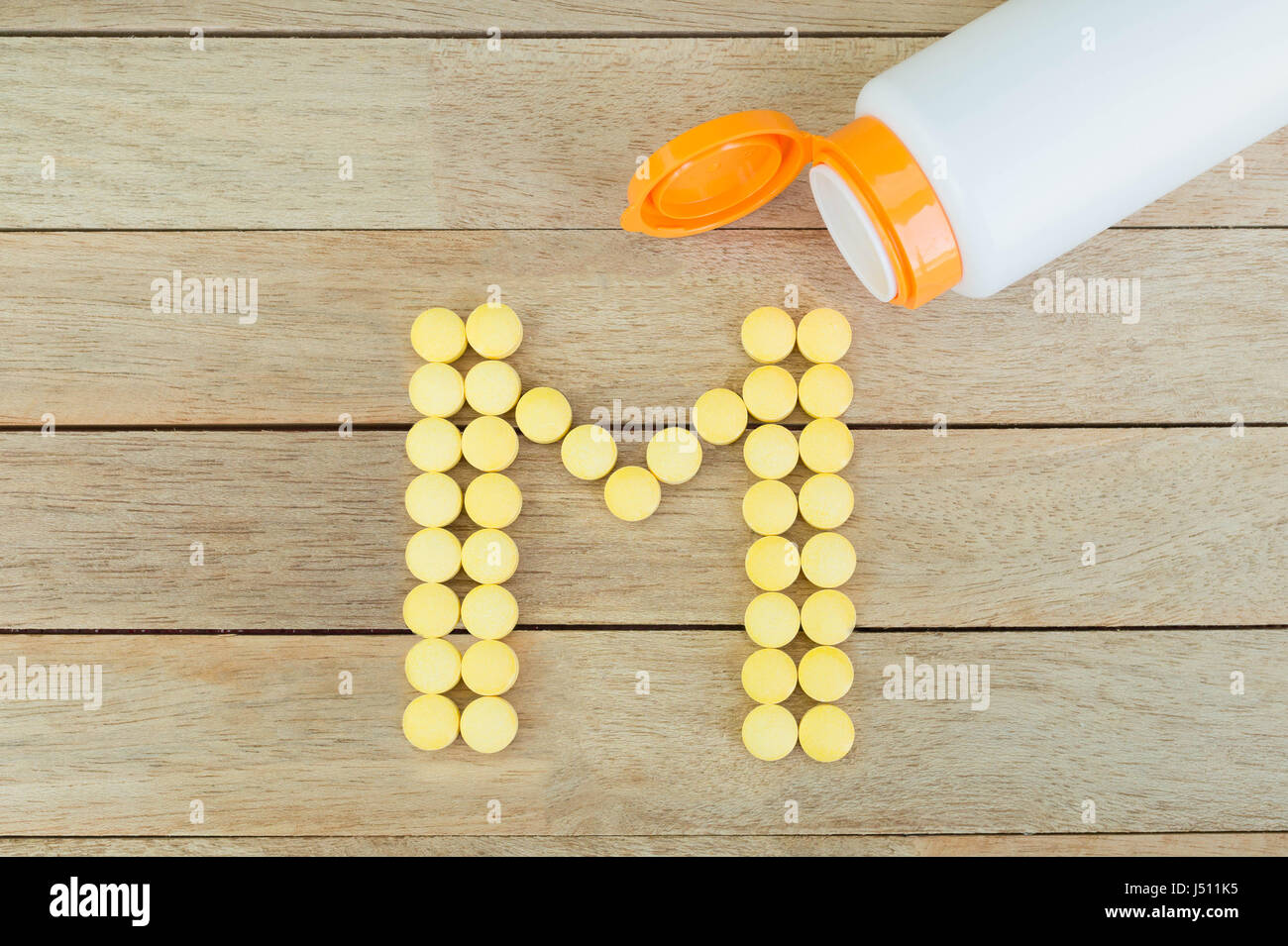 Yellow pills forming shape to M alphabet on wood background Stock Photo