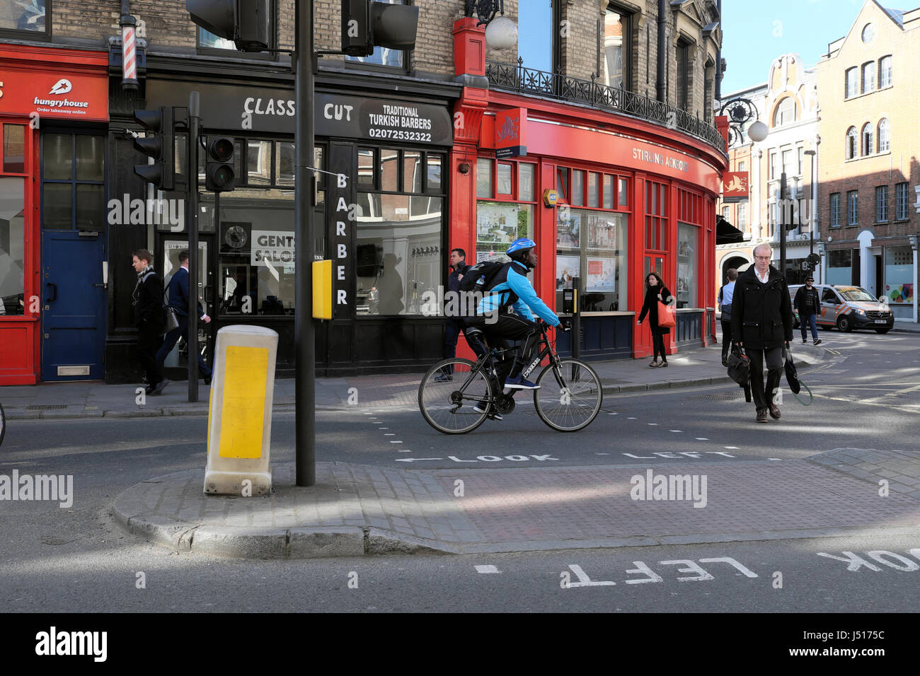 A man cycling to work cycle past small shops on the corner of St John Street and Clerkenwell Road in London EC1 UK   KATHY DEWITT Stock Photo