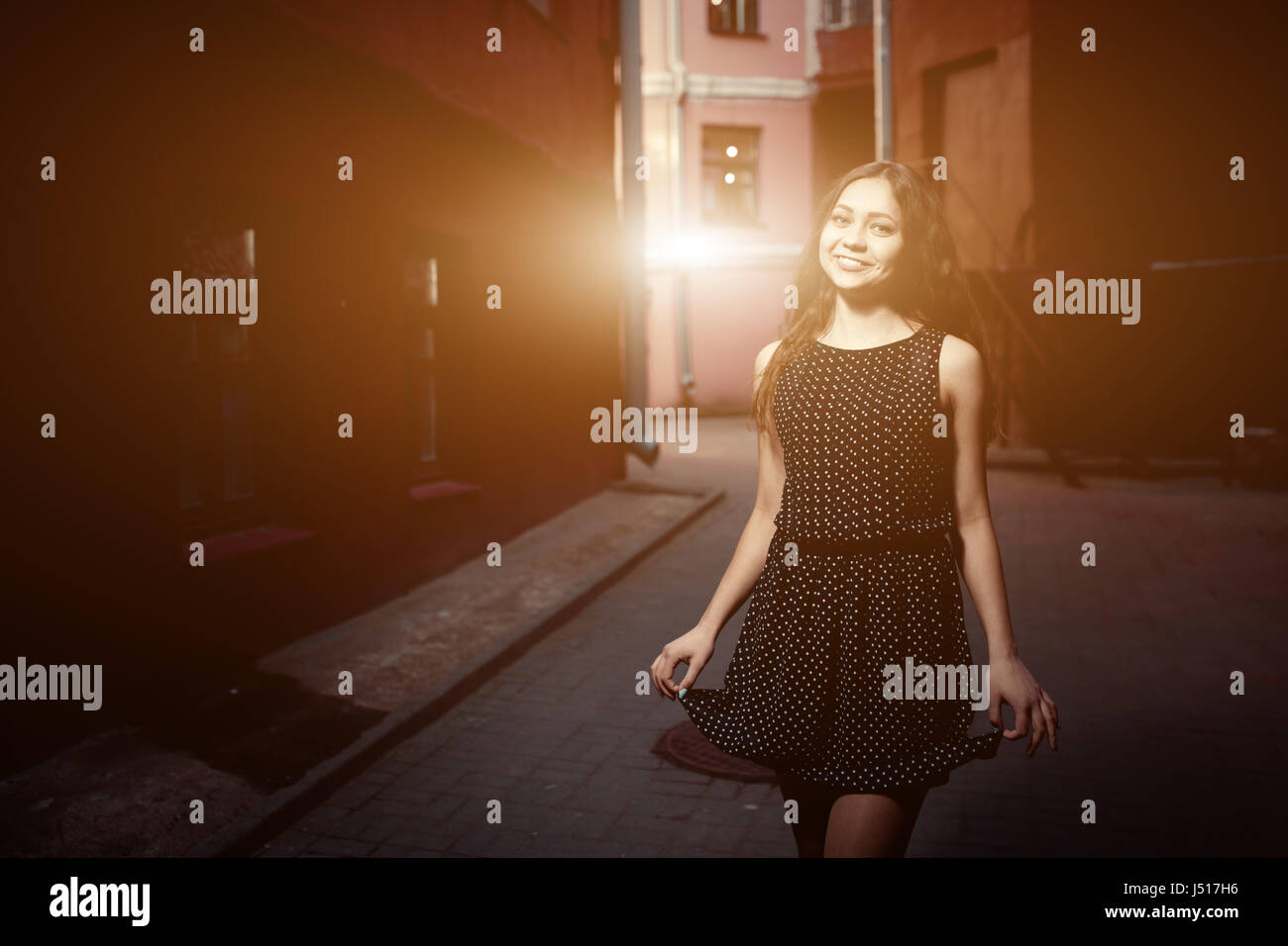 Beautiful brunette young woman wearing dress and walking on the street. Flare for text and design. Lifestyle in the city. Stock Photo