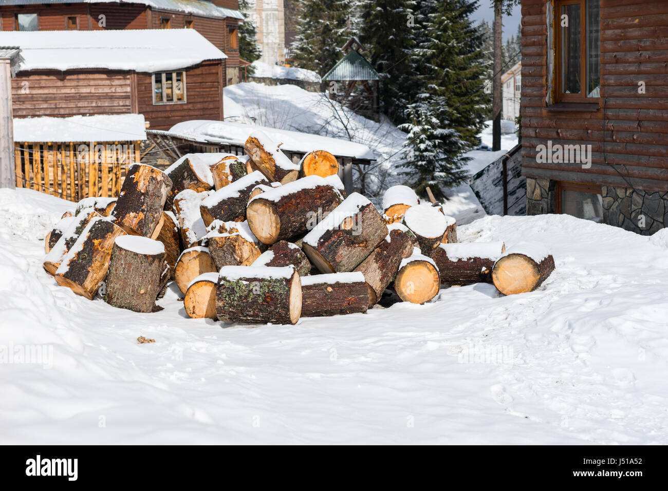 Stack of chopped fire woods on a snow near old wooden cottages Stock Photo
