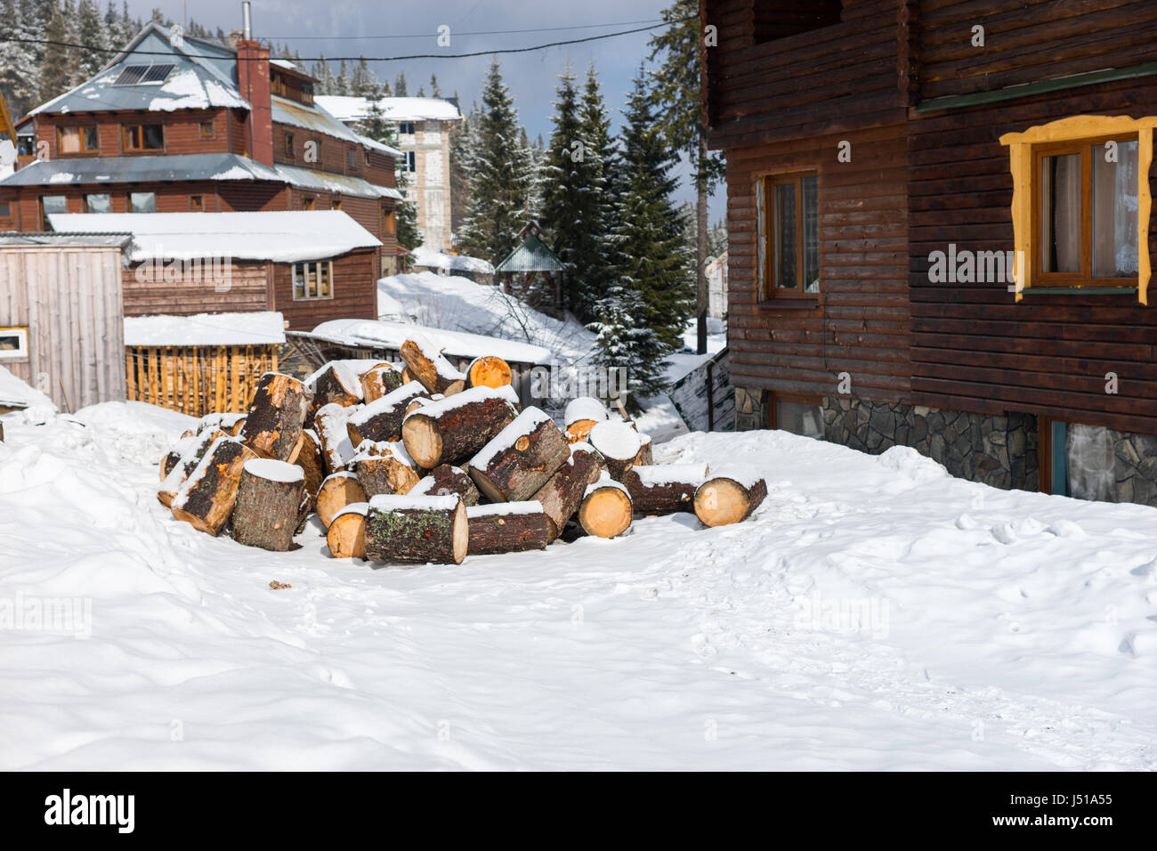 Stack of chopped woods on a snow near old wooden cottages Stock Photo