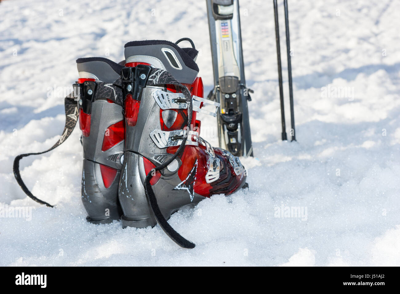 Close up of red and gray boots next to ski laying in fluffy snow in a ...
