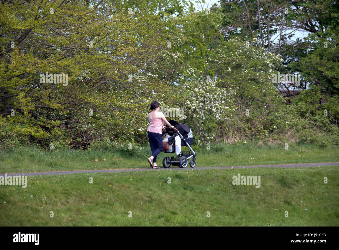 girl young mother pushing pram with baby on the Forth and Clyde canal towpath Glasgow Stock Photo
