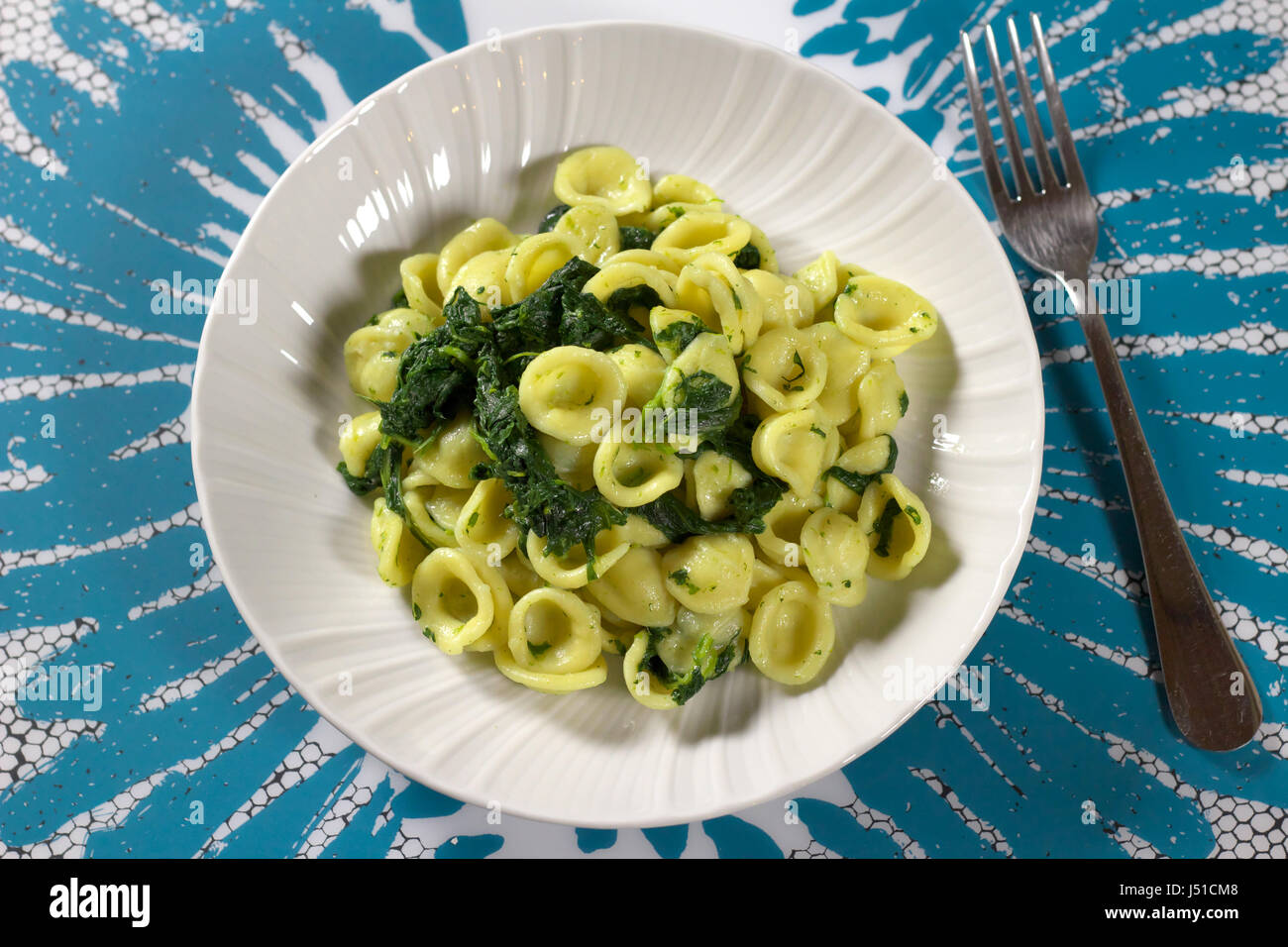 Turnip greens (collard greens) pasta (Italian Orecchiette alle cime di rapa) served in a white dish on white and light blue placemat - Direct above Stock Photo
