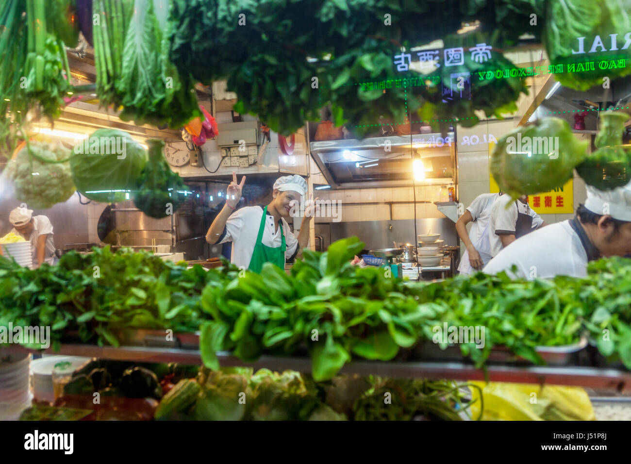 V-sign is given by a Malay restaurant chef through the window lined with green vegetables in Bukit Bintang, Kuala Lumpur, Malaysia. Stock Photo