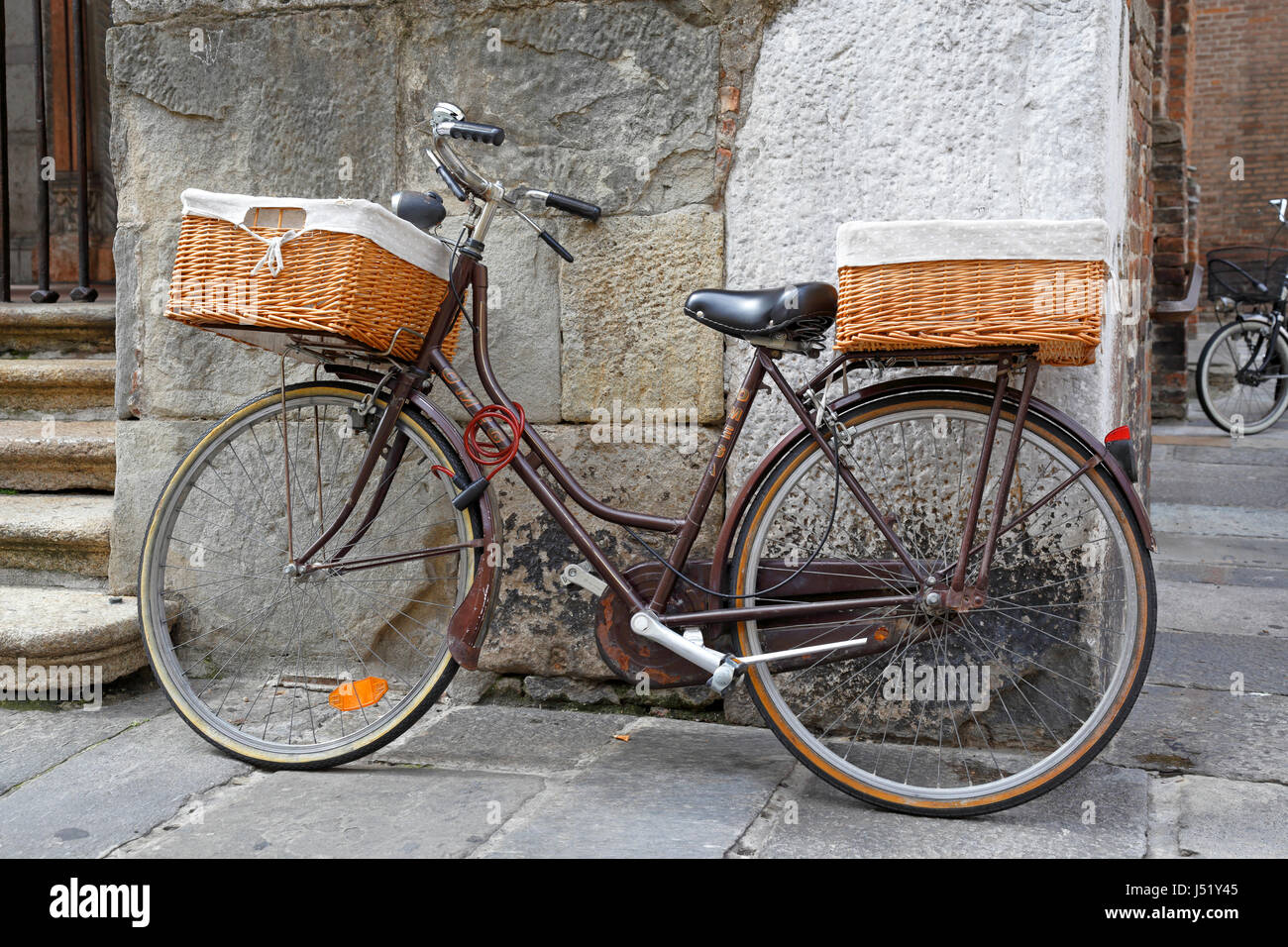 Old bicycle with wicker baskets leaning against an old stone building in Piacenza, Emilia-Romagna, Italy, Europe. Stock Photo