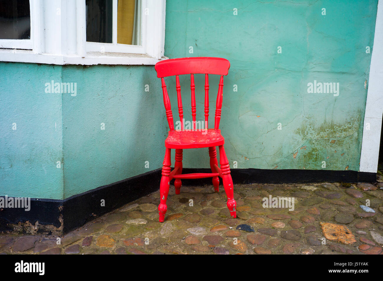 Thaxted Essex England UK. Salmon Pink chair outside house with green walls. May 2017 Stock Photo