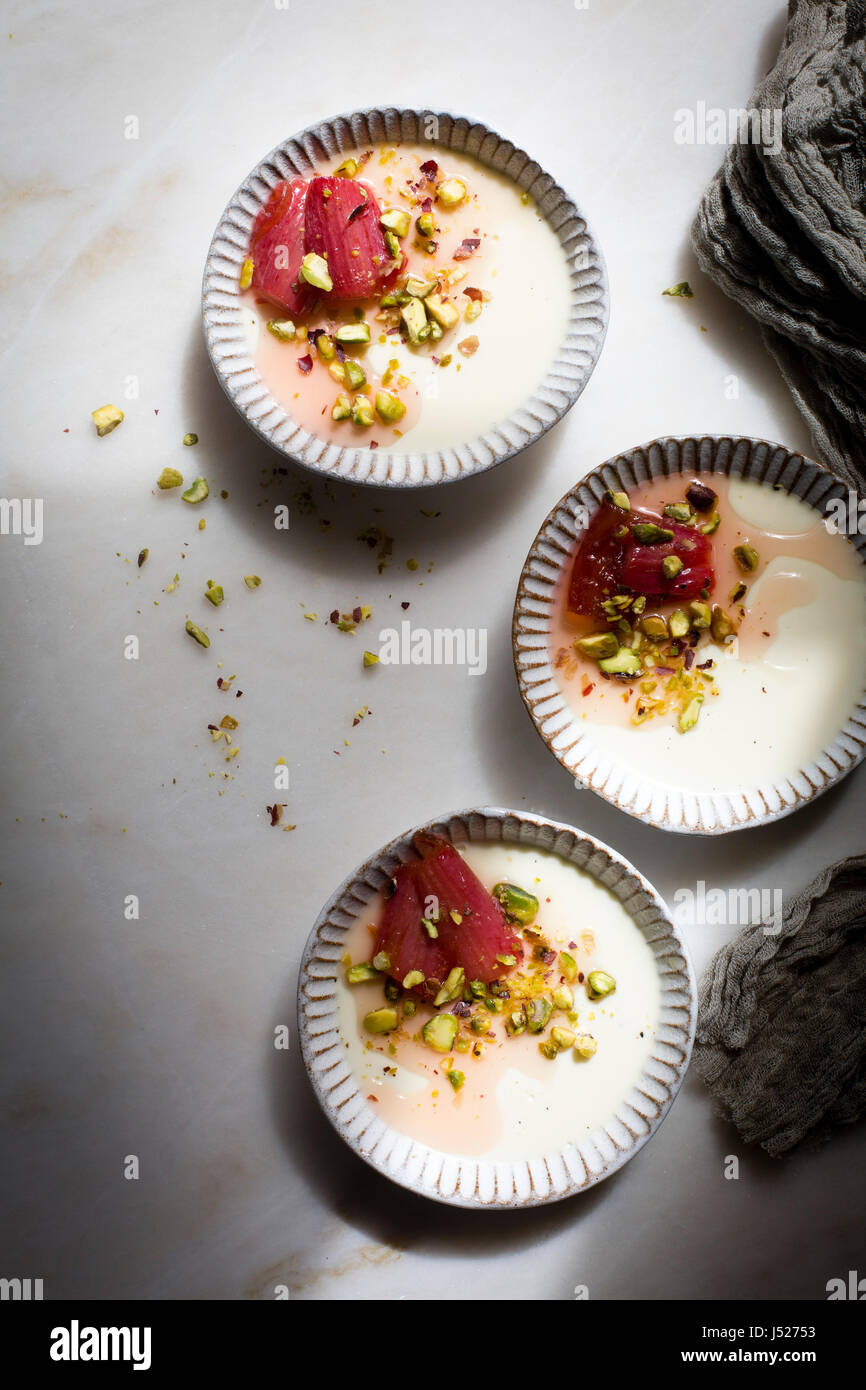 Classic vanilla pannacotta topped with roasted rhubarb and chopped pistachios in a ceramic tart pan on a marble table on top view Stock Photo