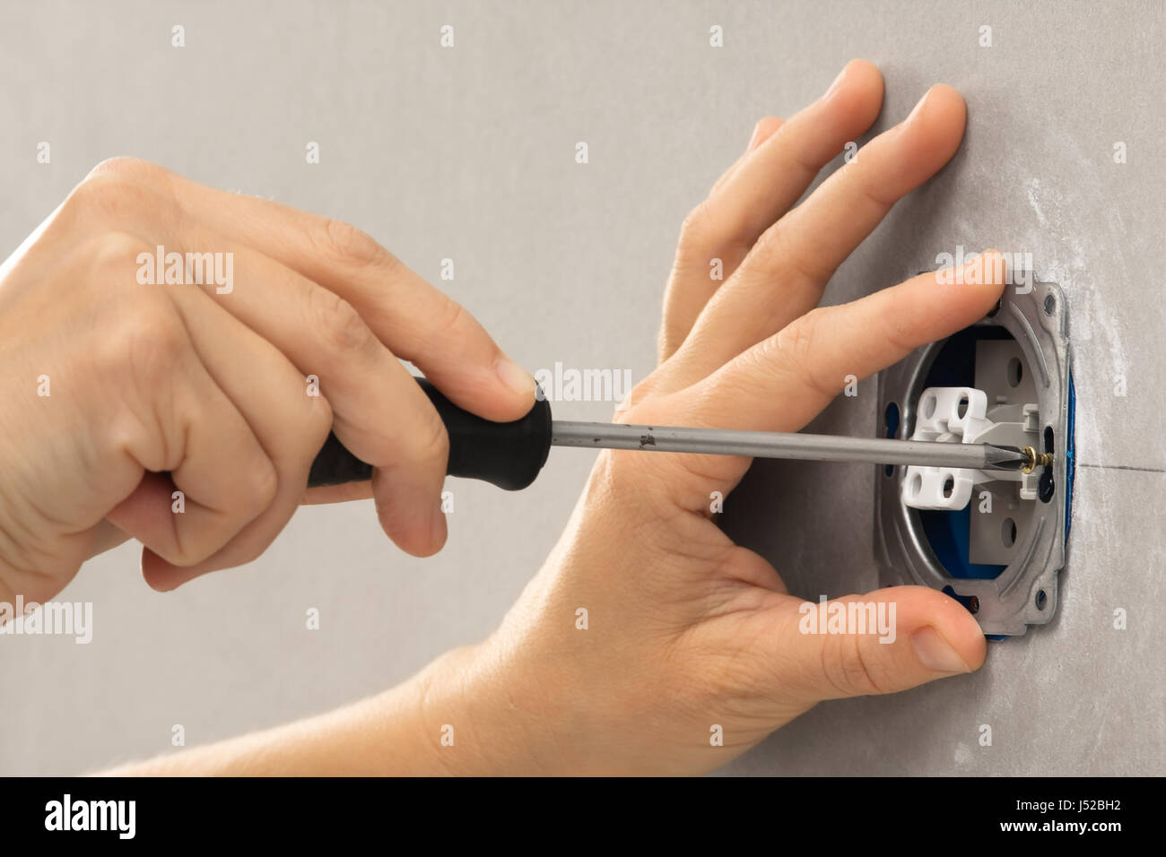 hands of electrician installing light switch with screwdriver in