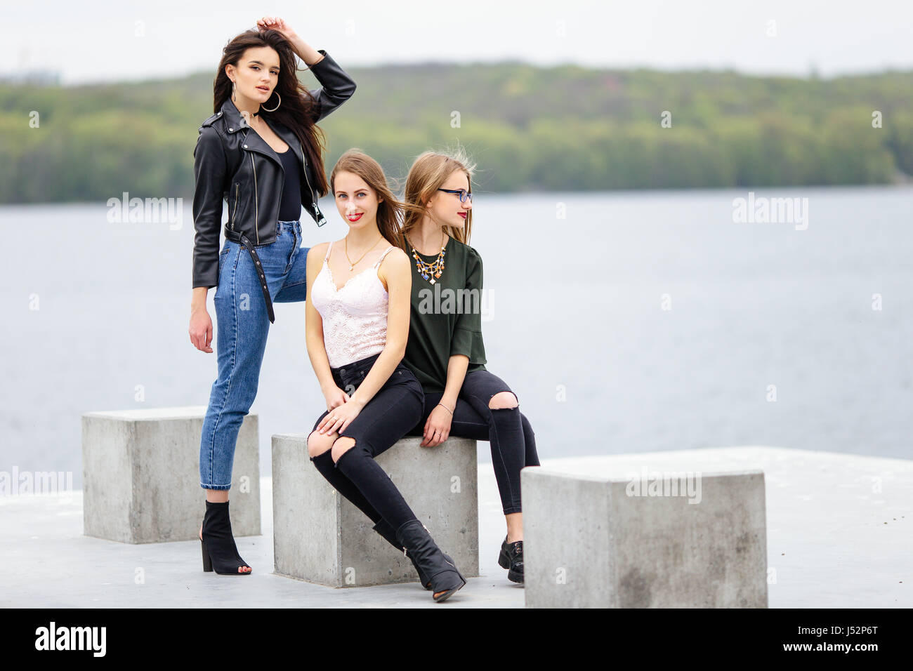 Two girls sit on bench with one stand near they, pose to camera Stock Photo