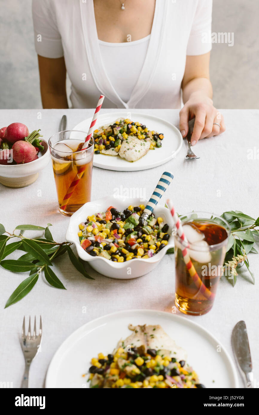A woman is photographed at a tablesetting with tilapia and black bean salsa in her plate. Stock Photo