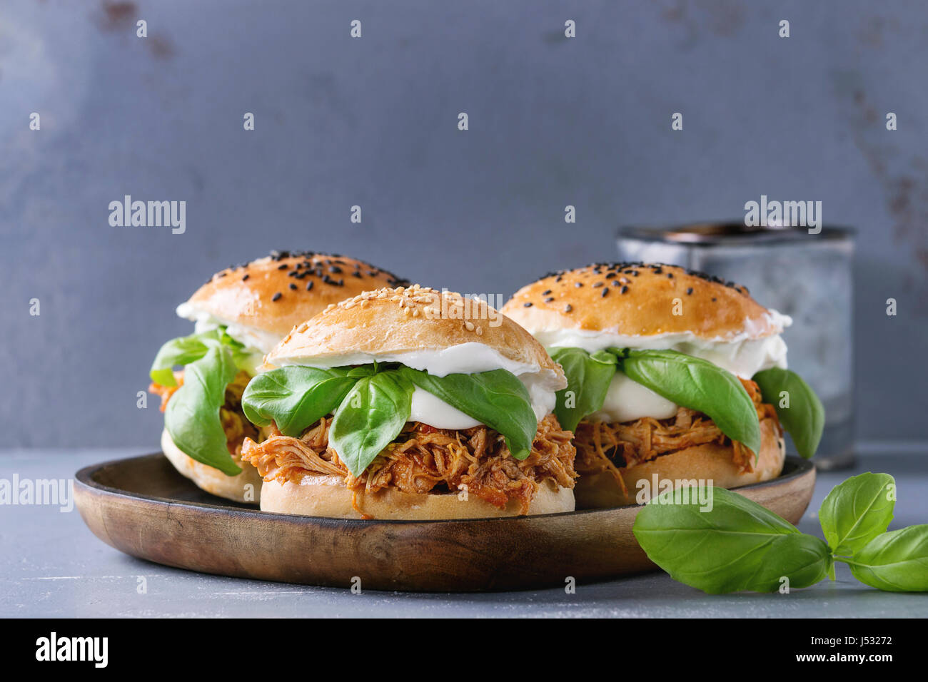 Homemade mini burgers with pulled chicken, basil, mozzarella cheese and yogurt sauce on wooden plate over gray texture background. Healthy fast food c Stock Photo