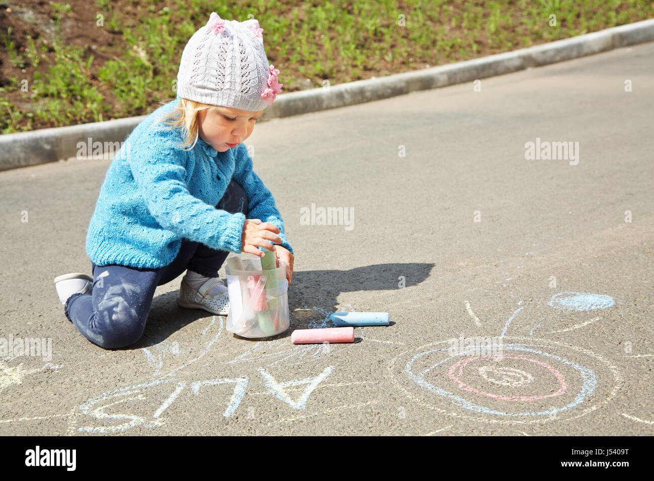 little girl draws chalk on asphalt. child playing in the open air in ...