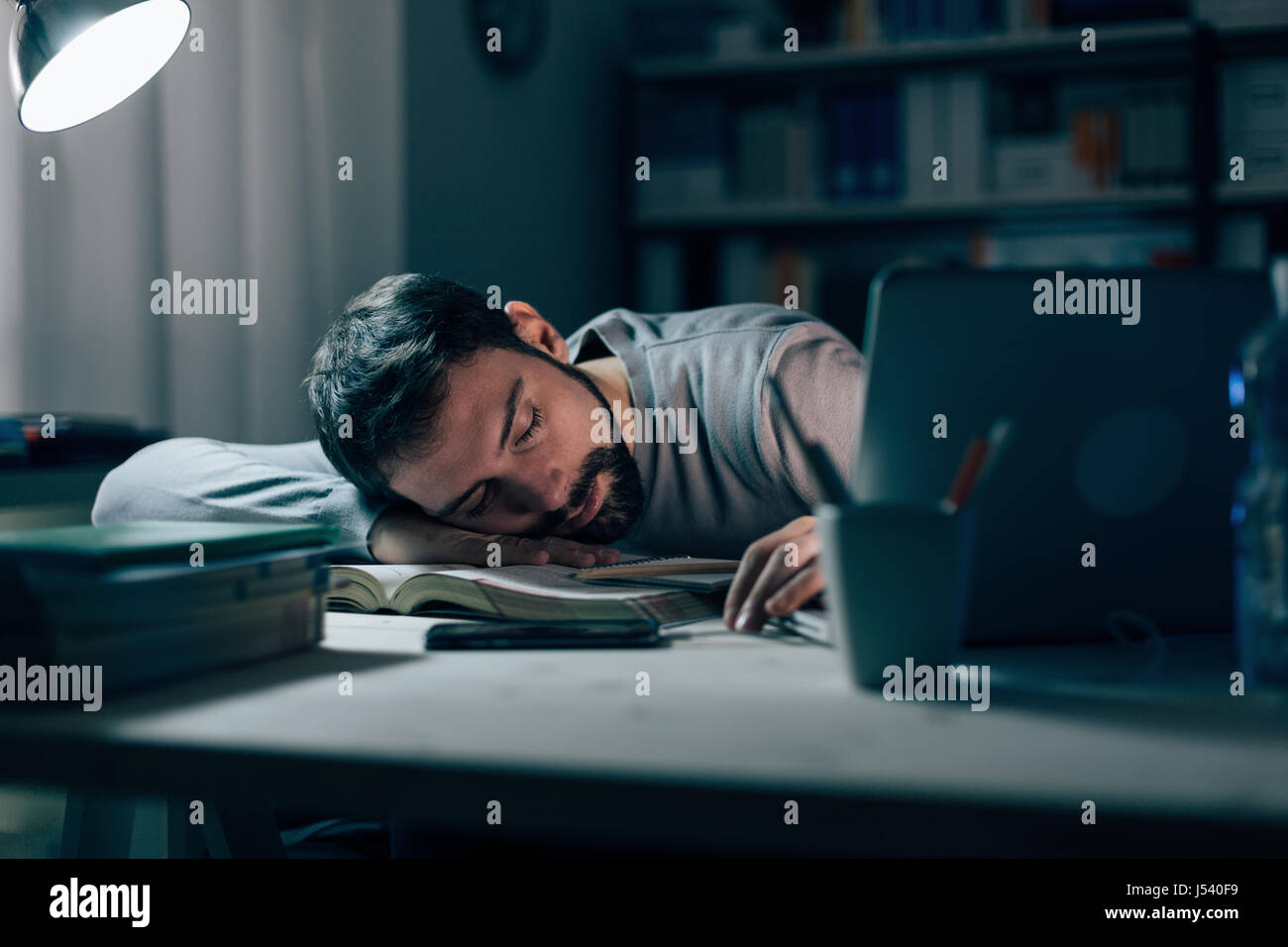 Young exhausted man in the office late at night sleeping on his desk on a book, restlessness and overwork concept Stock Photo