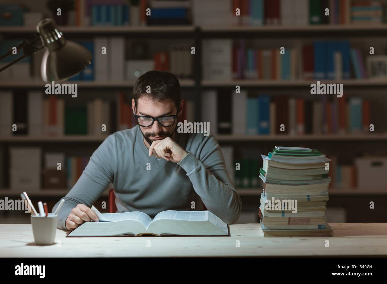Confident adult student at the library late at night, he is sitting at ...
