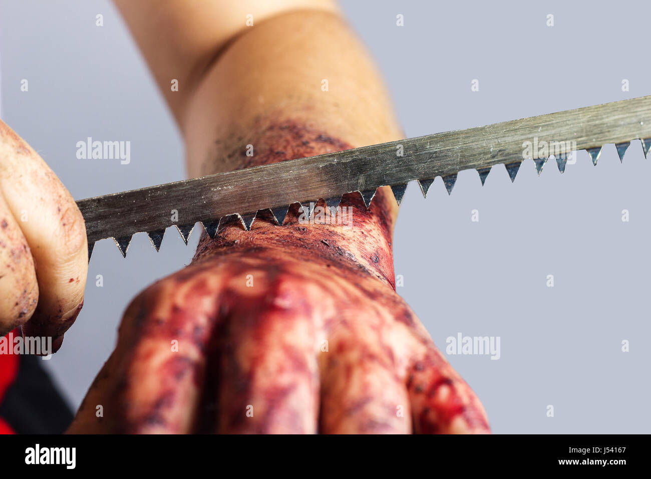 cutting into bloody hand with saw blade in front of grey background Stock Photo