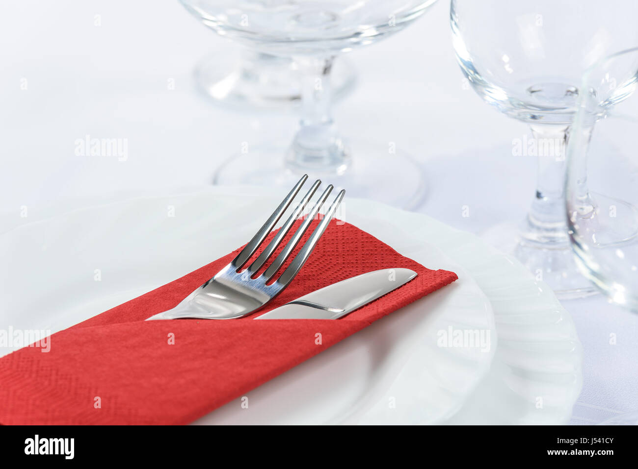 Elegant table setting in the restaurant: cutlery in a red napkin on the plates and next to the wine glasses Stock Photo