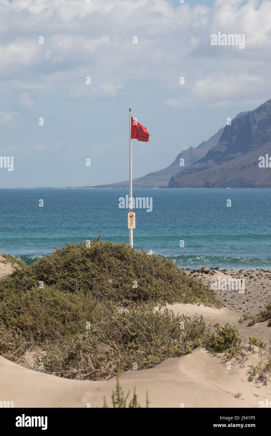 The red flag weighs in the wind at Surfers Beach Famara on Lanzarote. Stock Photo