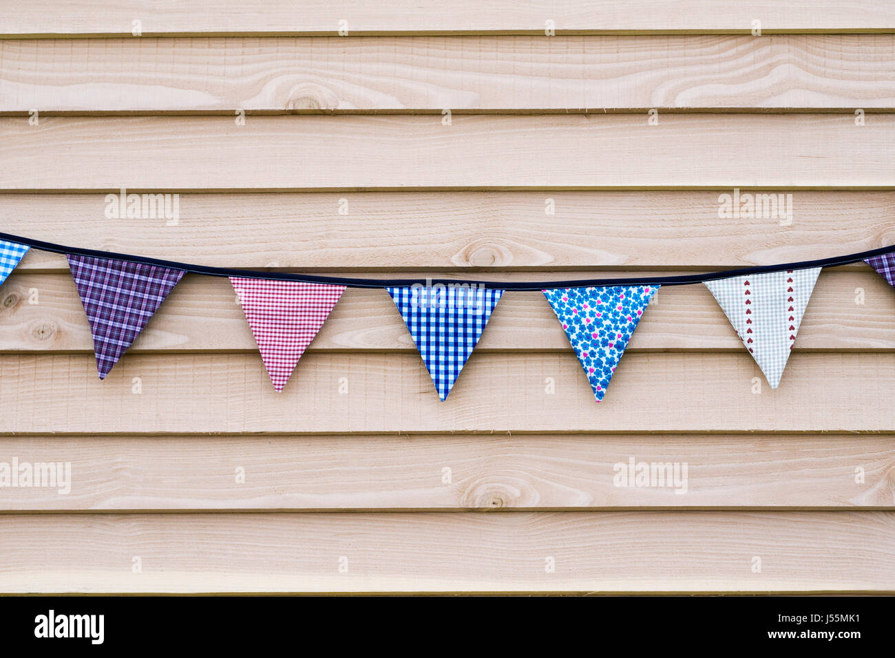 Colourful string of fabric bunting against a wooden panel Stock Photo