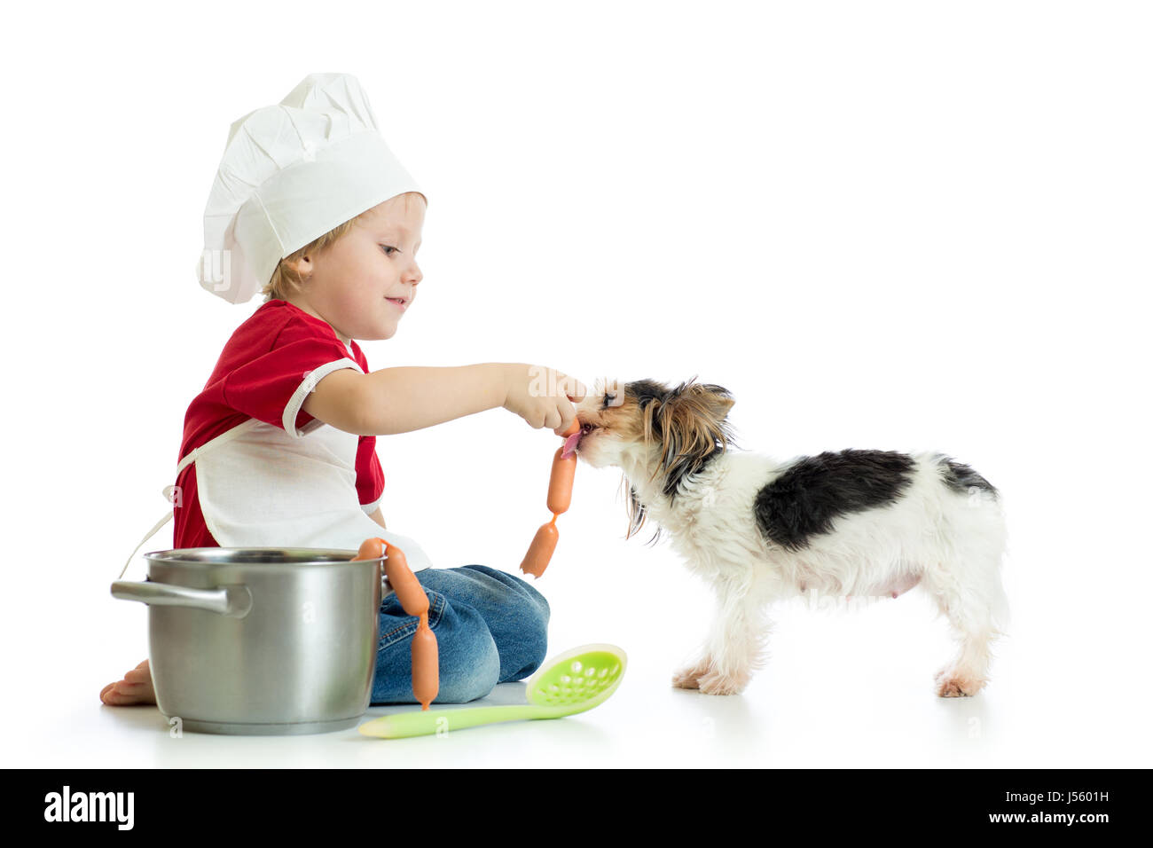 Role-playing game. Kid boy plays chef with pet. Child weared cook feeds dog. Stock Photo