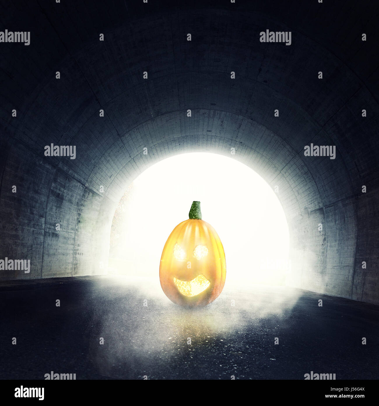 lighten jack-o-lantern in front of darken tunnel with fog and light at the end of tunnel Stock Photo