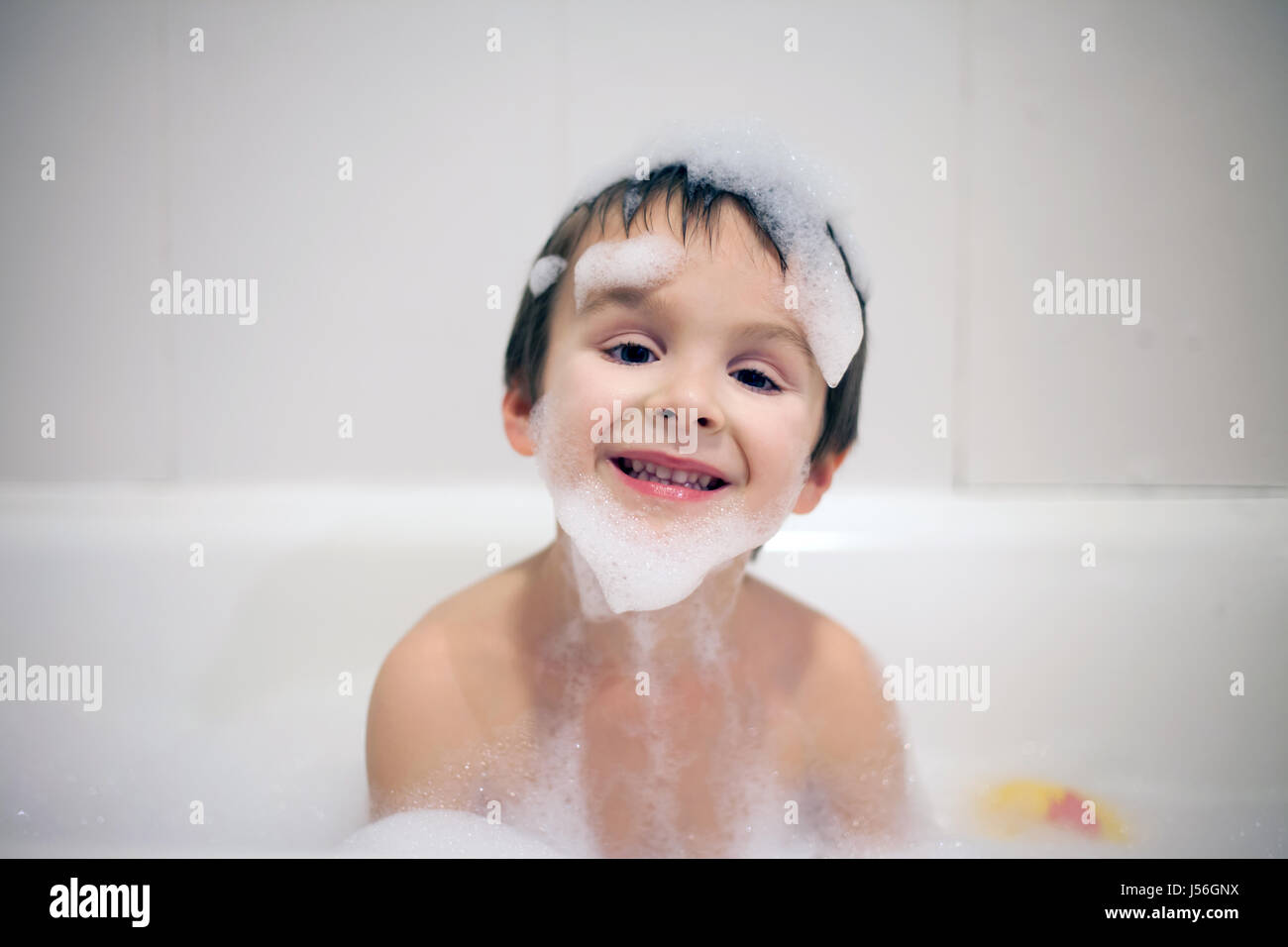 Cute boy in bathtub evening time, smiling, covered with soap foam Stock