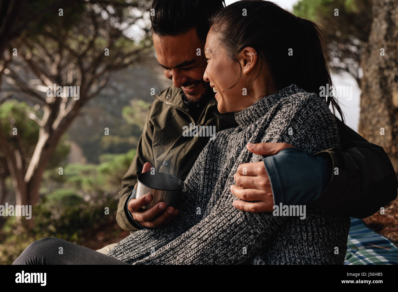 Young couple camping in countryside and having coffee. Young man and woman sitting together outdoors and smiling. Stock Photo