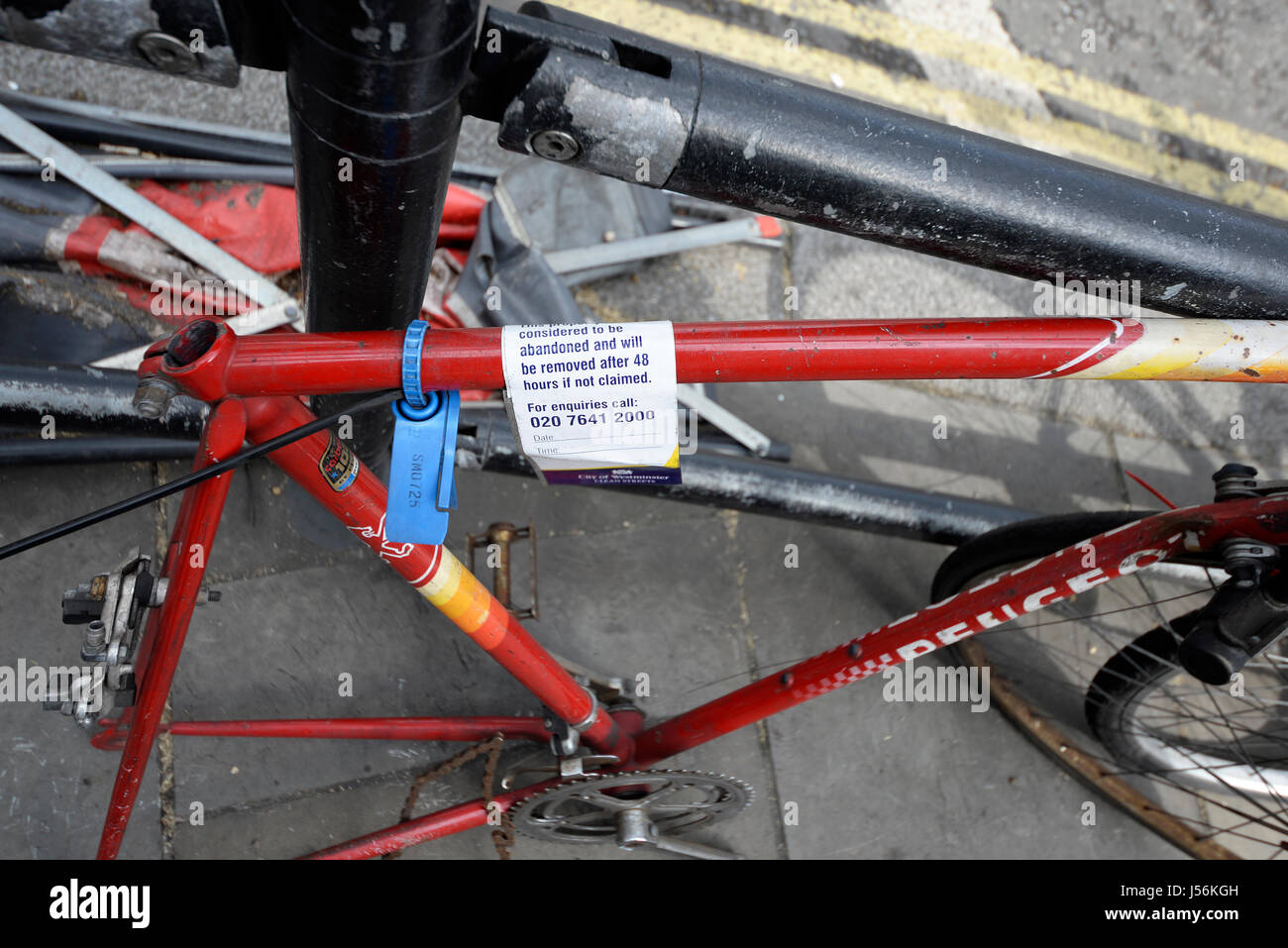 An abandoned bicycle chained to a railing near to Trafalgar Square in London with a warning that it will be removed by the City of Westminster Stock Photo