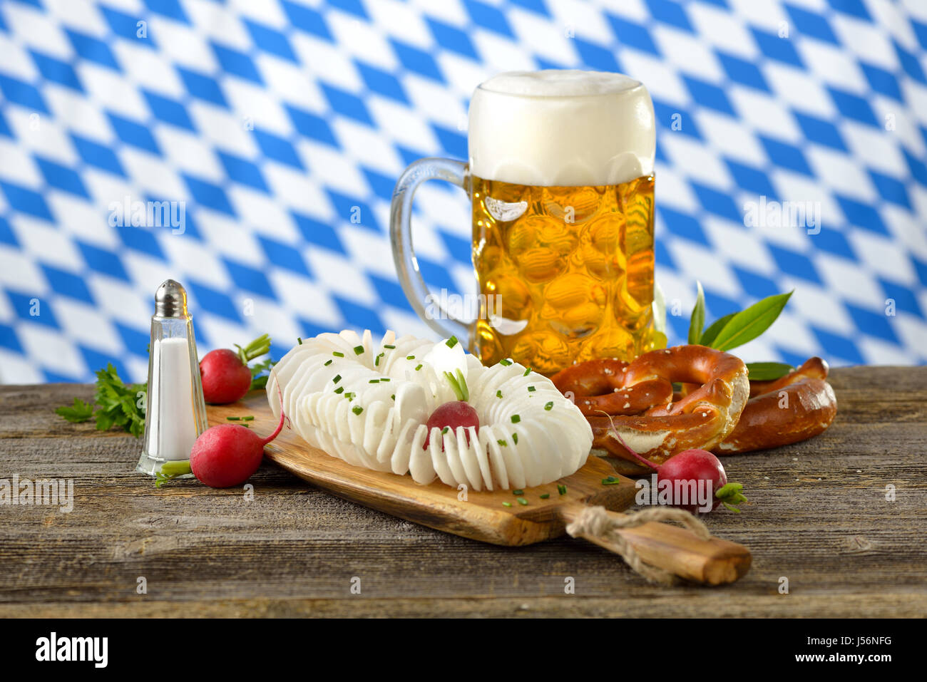 A typical Bavarian snack: Spirally cut and salted radish with pretzels and  Bavarian beer on a wooden table, in the background the white-blue flag Stock Photo
