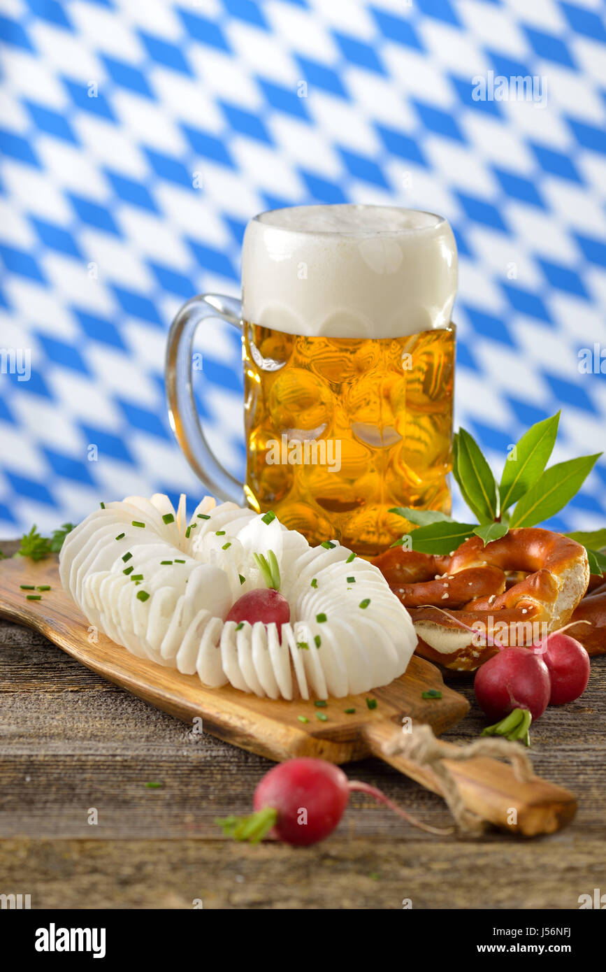 A typical Bavarian snack: Spirally cut and salted radish with pretzels and  Bavarian beer on a wooden table, in the background the white-blue flag Stock Photo