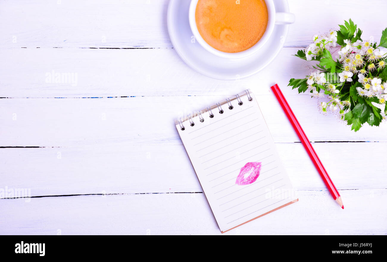 Paper notepad with a trace of a kiss from red lipstick, next cup of black coffee, empty space on the left Stock Photo