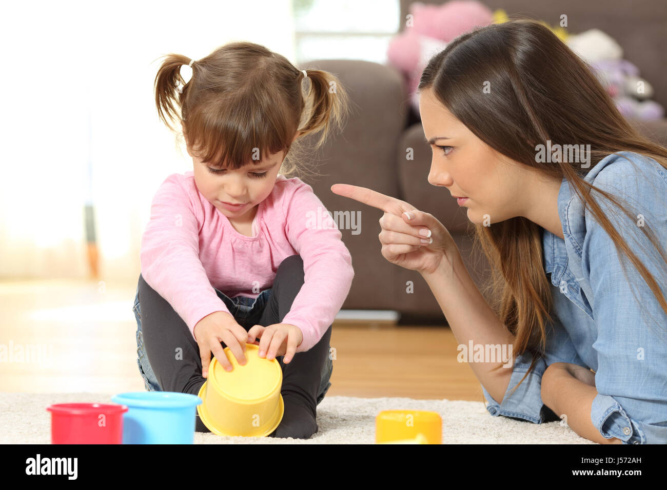 Portrait of a mother scolding to her baby daughter sitting on the floor in the living room at home Stock Photo