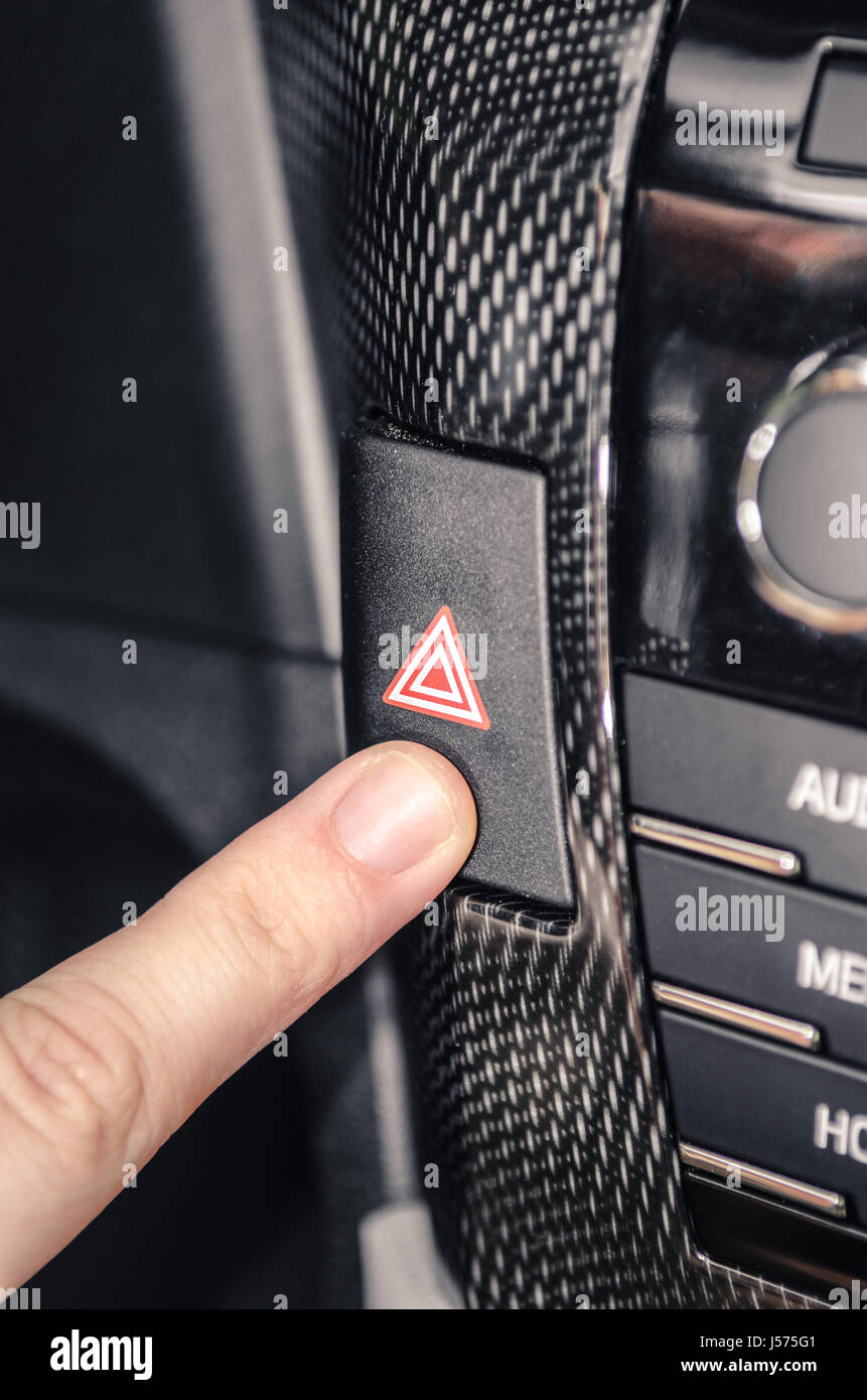 Finger pressing the car warning flashing button. Harzard switch Stock