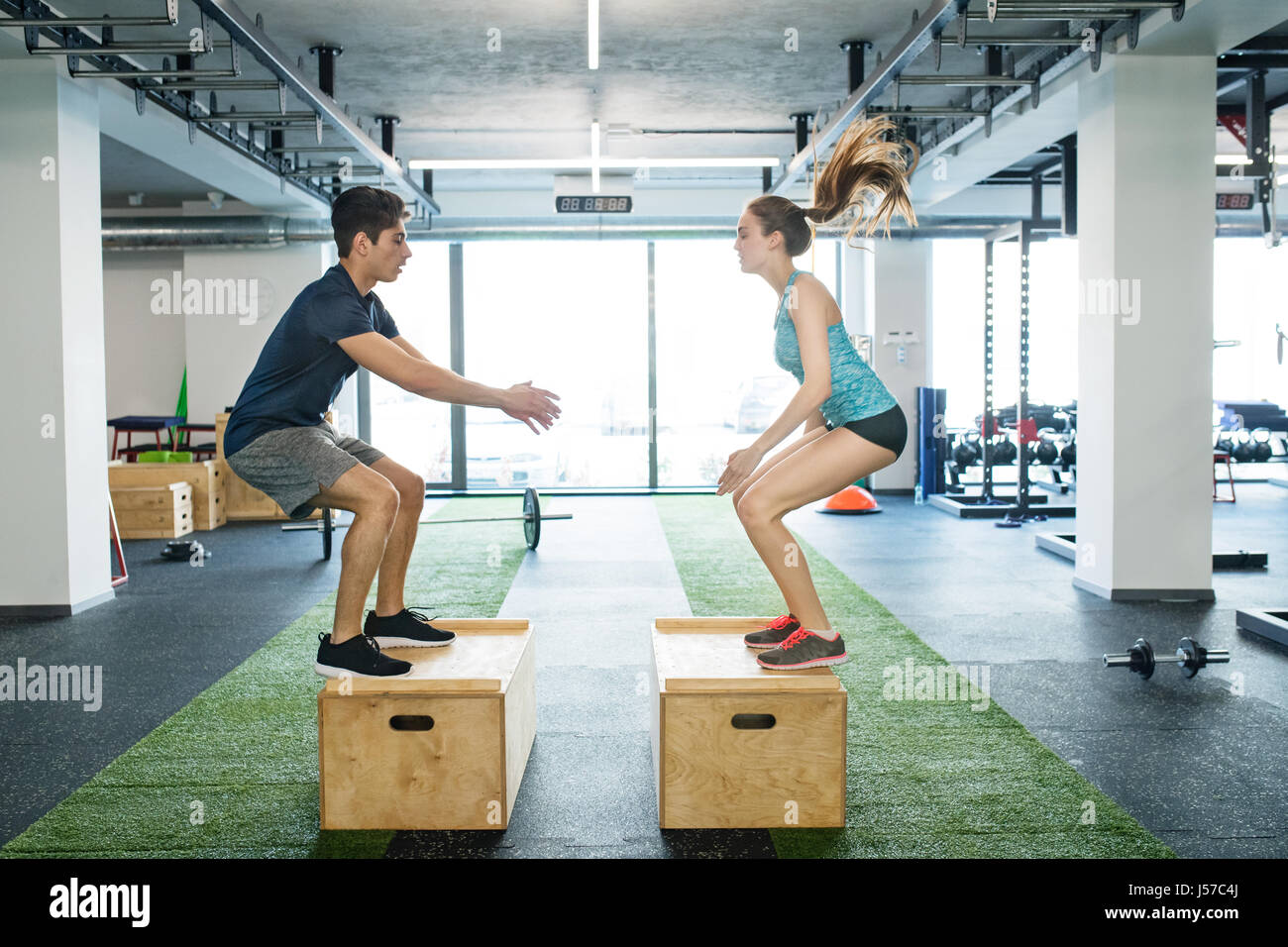 Young fit couple exercising in gym, doing box jumps. Stock Photo