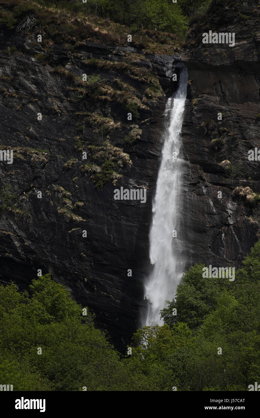 Water dripping down a tall mountain waterfall with lush vegetation,rocks and grass Stock Photo