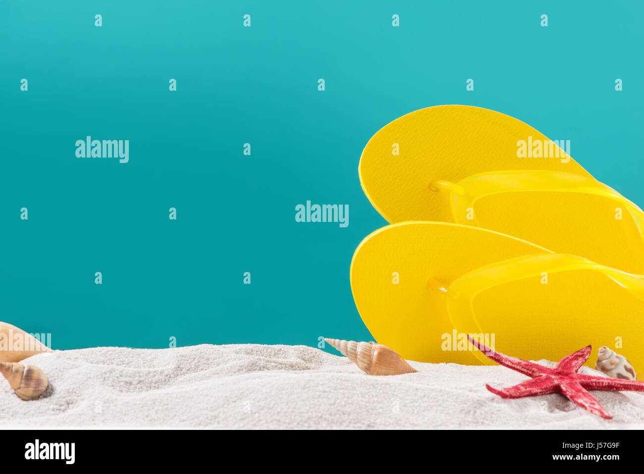 Yellow flip flops on beach against blue background Stock Photo - Alamy