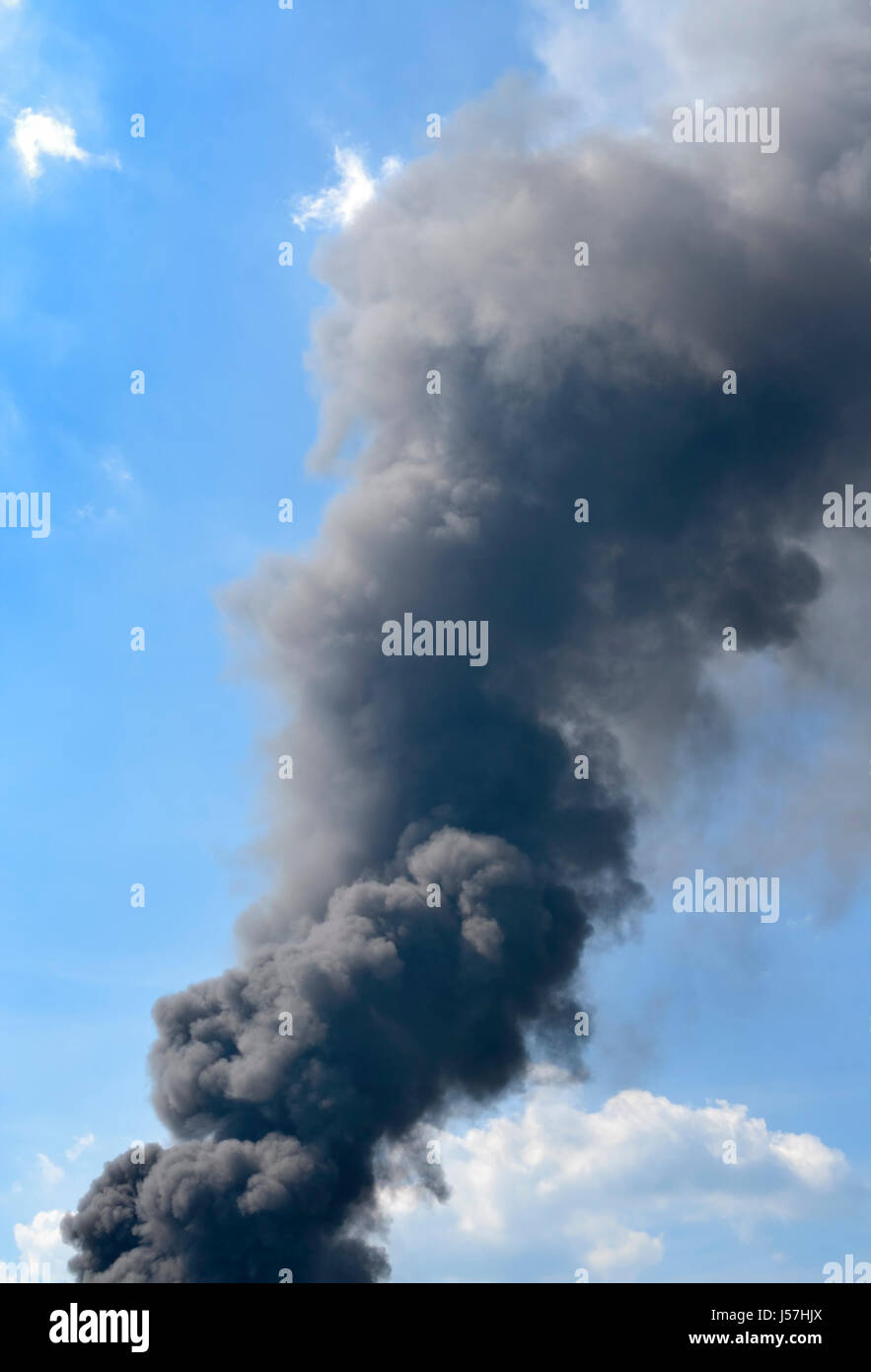 Thick dark smoke on blue sky with clouds Stock Photo