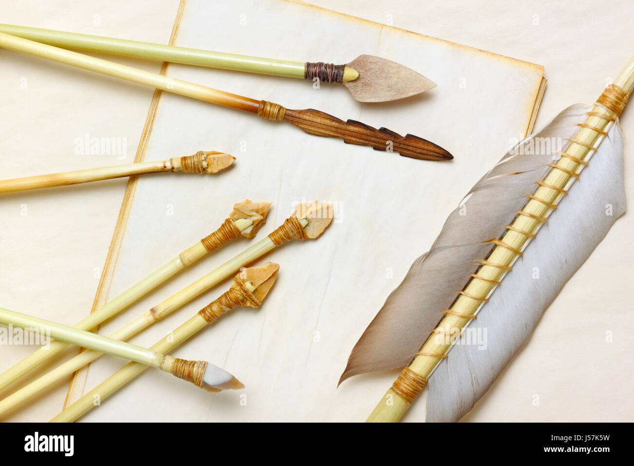 Primitive hunting and fishing arrows with flint stone, wood and bone arrowheads over aged paper sheets Stock Photo