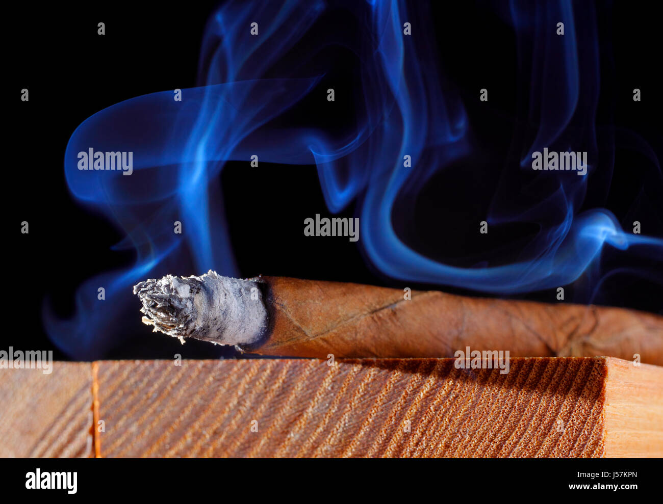 Cigar with abstract smoke. Wooden board, black background. Stock Photo