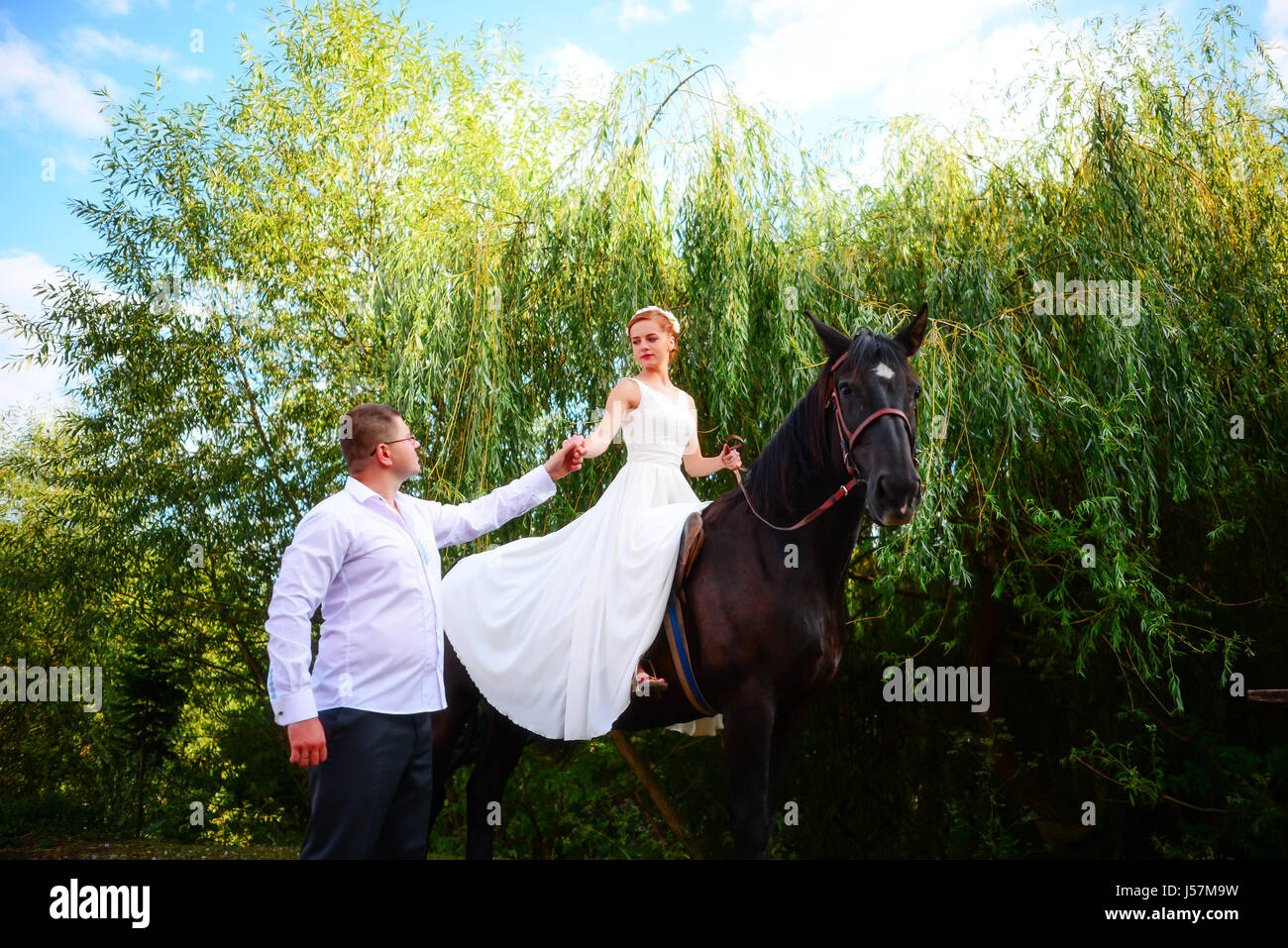 The groom leads the horse by the bridle. Bride sits in the saddle on