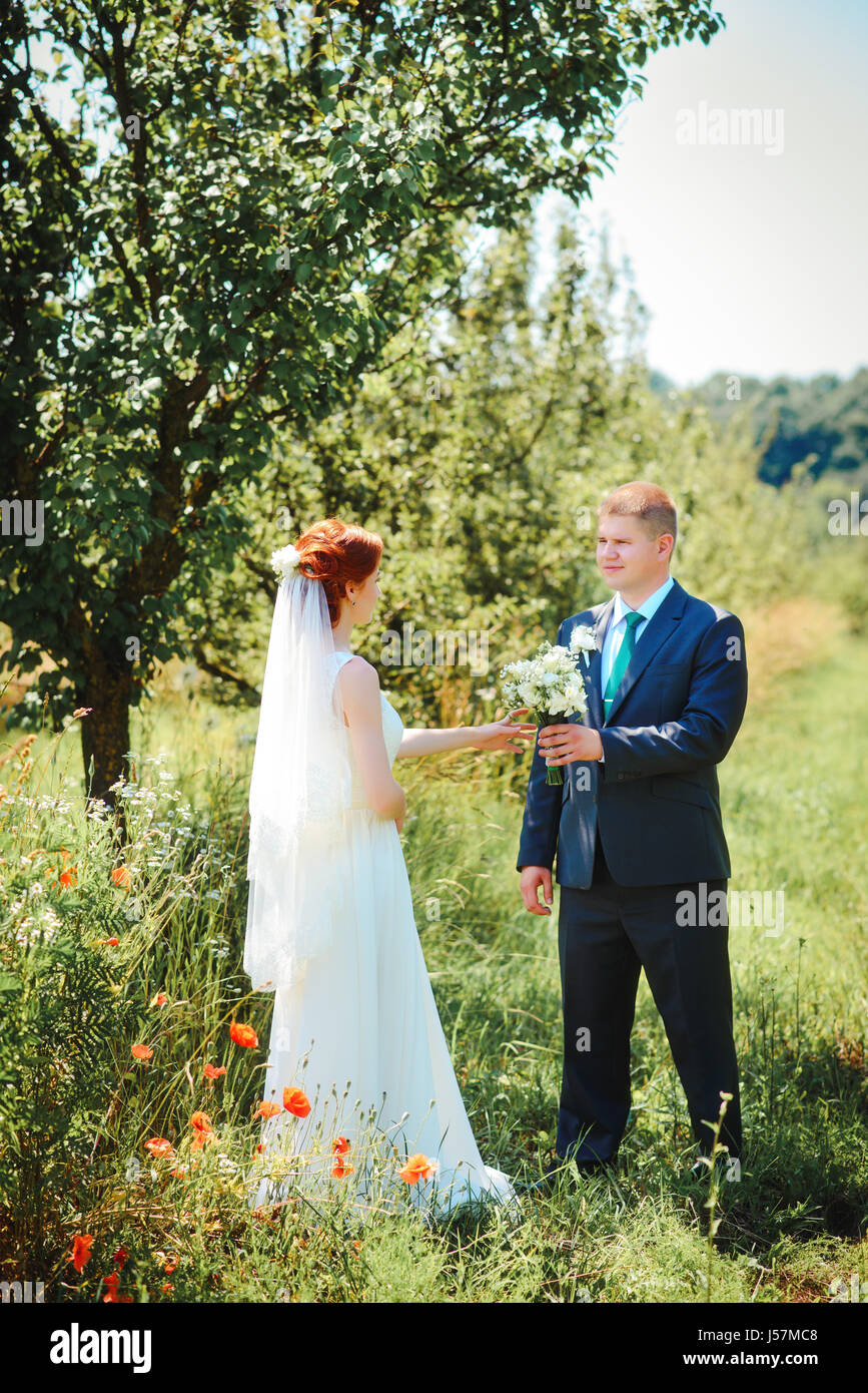 Bride and groom hold each other hands while they walk along the path in park Stock Photo