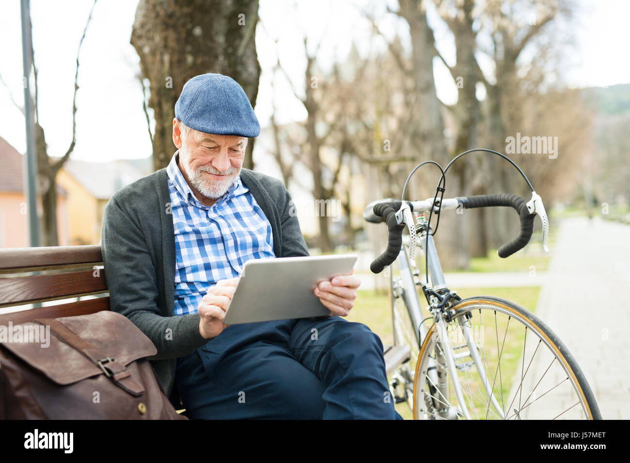 Senior man in town sitting on bench, working on tablet Stock Photo