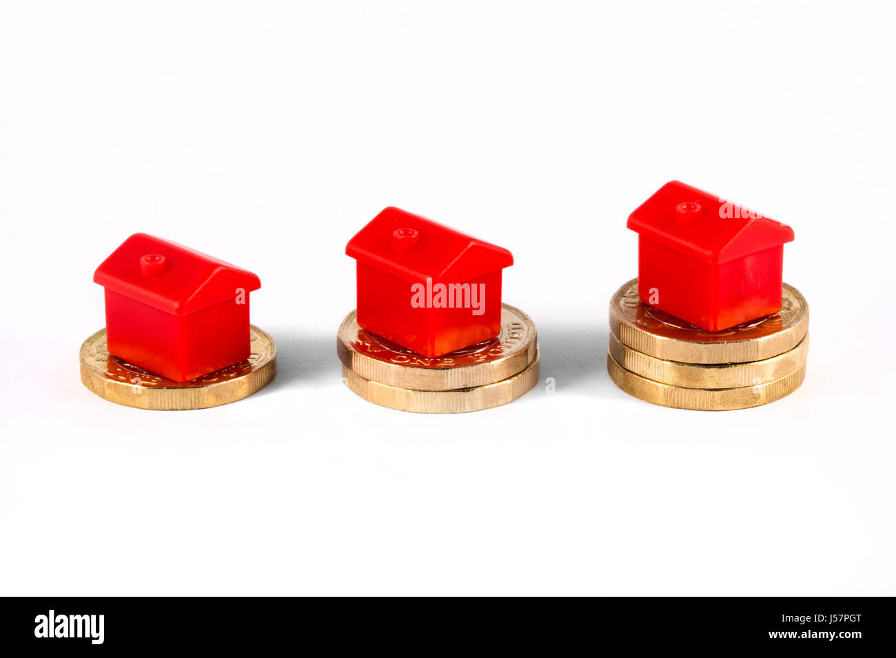 Red Houses sitting on top of stacks of coins, over a white background. Stock Photo