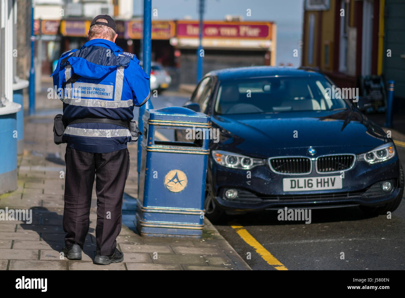 Parking Enforcement: A local authority employed  traffic warden issuing a ticket for a car parked on a solid yellow line Aberystwyth Wales UK Stock Photo