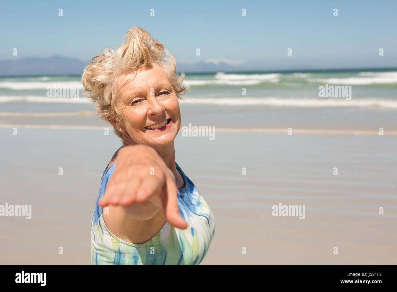 Portrait of smiling senior woman standing against clear sky at beach ...