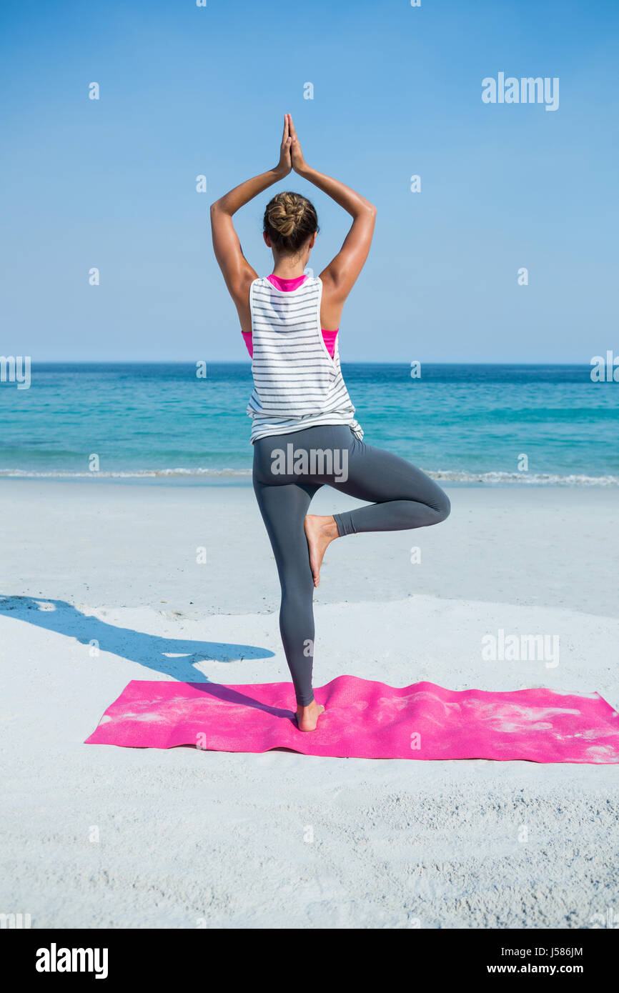 Rear view of woman practicing yoga in tree pose at beach on sunny day ...